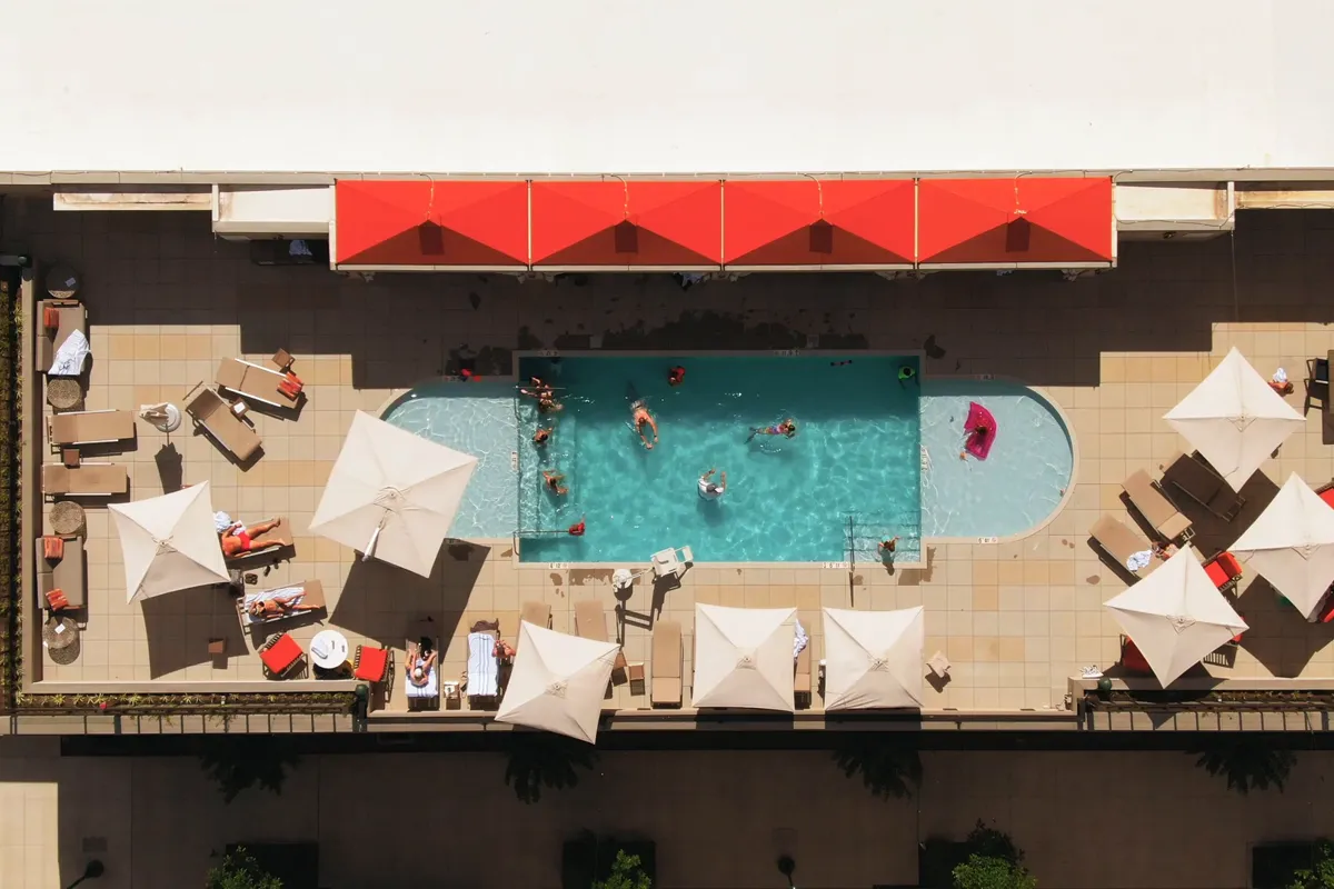 Aerial view of a hotel pool with guests swimming between white umbrellas